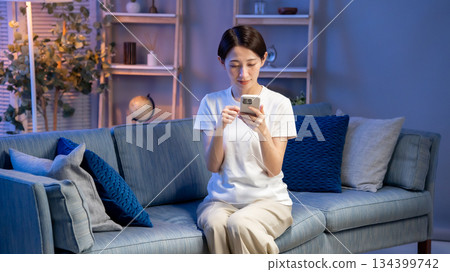 A woman looking at her smartphone in the living room A woman looking at her smartphone in the living room 134399742