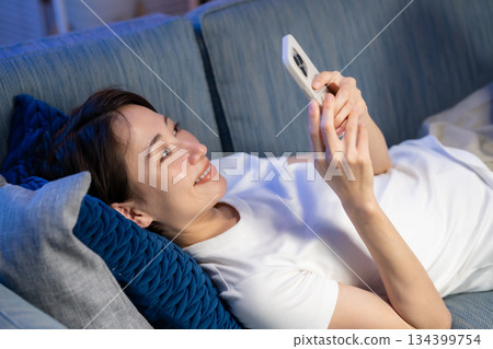一位女士躺在沙發上看著她的智慧型手機 134399754