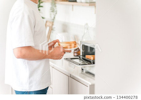 亞洲年輕男子在廚房的烤麵包機裡烤麵包 134400278