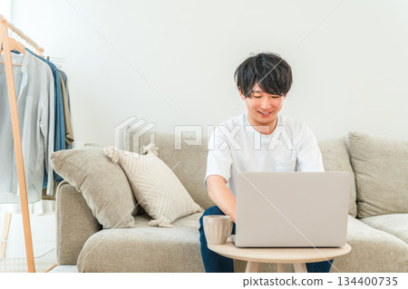 A young Asian man sitting on a sofa and using a laptop 134400735