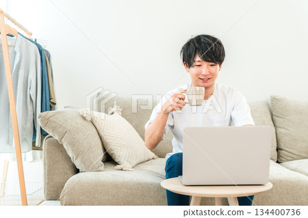 A young Asian man sitting on a sofa and using a laptop 134400736