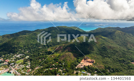 Aerial view of a verdant island with vibrant green vegetation and turquoise waters lapping at its rocky coastline. Praslin, Seychelles. Aerial view of a verdant island with vibrant green vegetation and turquoise waters lapping at its rocky coastline. Praslin, Seychelles. 134401568