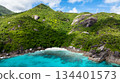 A small, secluded sandy beach bordered by lush green hills, leading to clear turquoise waters. Seychelles, Mahe. 134401573