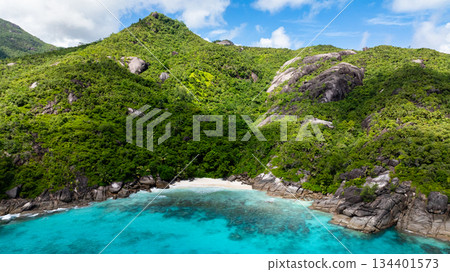 A small, secluded sandy beach bordered by lush green hills, leading to clear turquoise waters. Seychelles, Mahe. 134401573