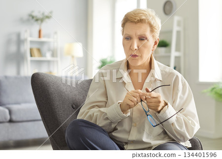 Thoughtful And Sad Elderly Woman Sitting At Home In Despair Thoughtful And Sad Elderly Woman Sitting At Home In Despair 134401596