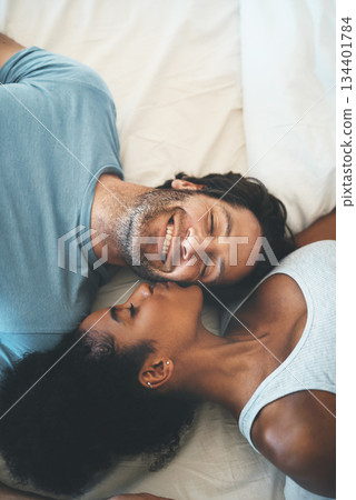 Happy interracial couple, kiss and relax on bed above for morning bonding, intimate relationship or love at home. Top view of woman kissing man lying in bedroom for loving romance, care or affection 134401784