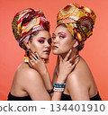 African fashion, cosmetics and portrait of women on orange background with accessory, makeup and beauty. Glamour, luxury and female people in exotic jewelry, traditional style and scarf in studio 134401910