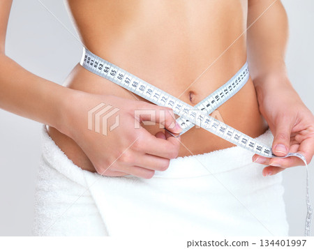 Woman, hands and tape measure on stomach for lose weight, diet or slim body against a grey studio background. Hand of female person or model measuring waist in weightloss, results or healthy wellness 134401997