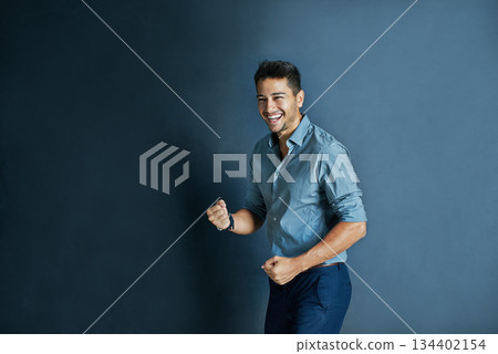 Celebration, fist pump and portrait of a businessman in a studio with achievement or winning. Happy, smile and professional male employee winner with success to celebrate isolated by blue background. Celebration, fist pump and portrait of a businessman in a studio with achievement or winning. Happy, smile and professional male employee winner with success to celebrate isolated by blue background. 134402154