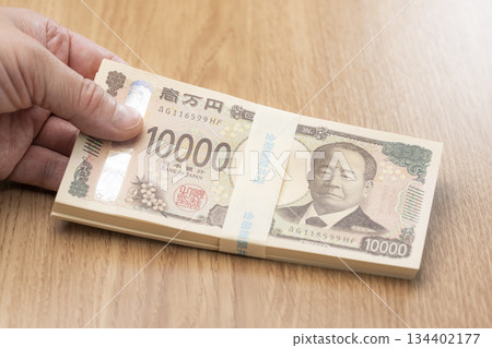 Image of a large amount of Japanese yen holding a stack of 10,000 yen bills Image of a large amount of Japanese yen holding a stack of 10,000 yen bills 134402177