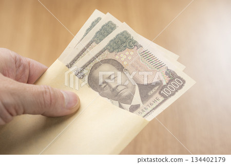 A hand taking out a 10,000 yen bill from an envelope shows an image of paying in Japanese yen 134402179