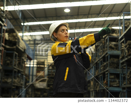 Hispanic female foreman worker holding walkie talkie, checking inventory of auto parts and engine maintenance duties in factory. Hispanic female foreman worker holding walkie talkie, checking inventory of auto parts and engine maintenance duties in factory. 134402372
