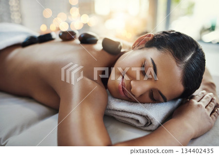 Happy woman, relax and sleeping on bed at spa for rock massage, skincare or beauty treatment indoors. Calm female asleep with eyes closed and smile for hot rocks on back or body care at the resort 134402435