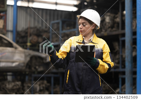 Hispanic female foreman worker standing holding tablet, checking inventory of auto parts and engine maintenance duties in factory. 134402509