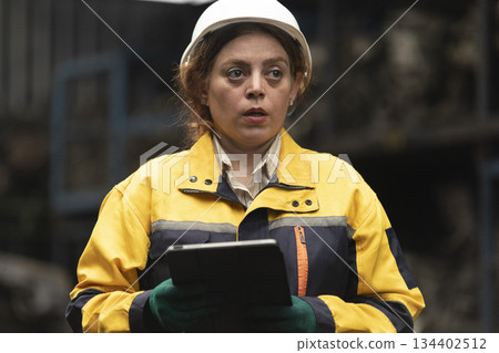 Hispanic female foreman worker standing holding tablet, checking inventory of auto parts and engine maintenance duties in factory. Hispanic female foreman worker standing holding tablet, checking inventory of auto parts and engine maintenance duties in factory. 134402512