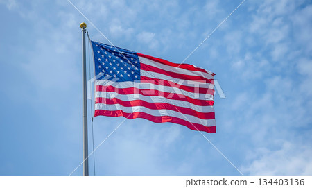American Flag Flown On Tall Flagpole Against Clear Blue Sky, Symbol Of Freedom And Patriotism 134403136