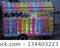 Colorful cotton candy bags are neatly arranged on a cart, with backlighting to highlight the pastel colors, creating a lively street stall. 134403223