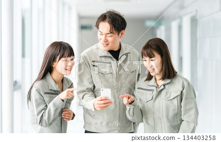 Male and female staff in the manufacturing, building, transportation and construction industries wearing work clothes talking while looking at their smartphones 134403258
