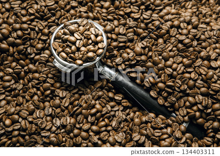 Portafilter Filled With Roasting Coffee Beans Amidst Evenly Scattered Coffee Beans on Surface 134403311