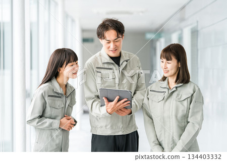 Male and female staff in the manufacturing, building, transportation and construction industries wearing work clothes talking while looking at a tablet 134403332