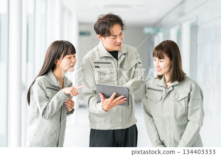 Male and female staff in the manufacturing, building, transportation and construction industries wearing work clothes talking while looking at a tablet 134403333