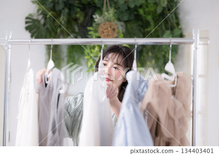 一位年輕女性面帶微笑地挑選衣服,展現她時尚的生活方式。她正在欣賞各種衣服。 一位年輕女性面帶微笑地挑選衣服,展現她時尚的生活方式。她正在欣賞各種衣服。 134403401