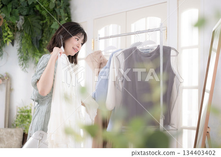 一位年輕女性帶著微笑挑選衣服，展現她充滿少女氣息的時尚生活方式。 134403402