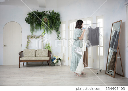 Fashion lifestyle of a young woman picking up clothes and choosing them with a smile, looking in the mirror Fashion lifestyle of a young woman picking up clothes and choosing them with a smile, looking in the mirror 134403403