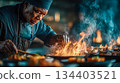 A chef in the kitchen prepares a dish over an open fire. Ingredients are nearby. Flame, heat, and action 134403521