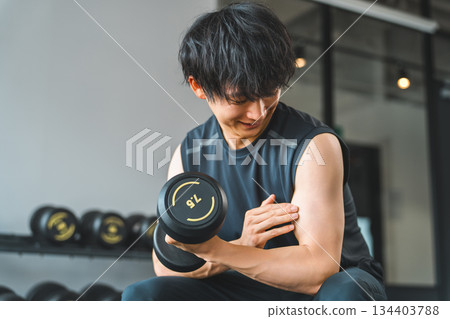 一名年輕的亞洲男子在健身房進行啞鈴訓練。 134403788