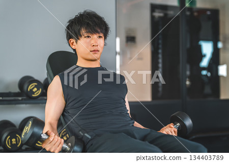 一名年輕的亞洲男子在健身房進行啞鈴訓練。 134403789