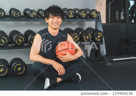 年輕亞裔男子在健身房裡拿著籃球和舉重球 年輕亞裔男子在健身房裡拿著籃球和舉重球 134404236