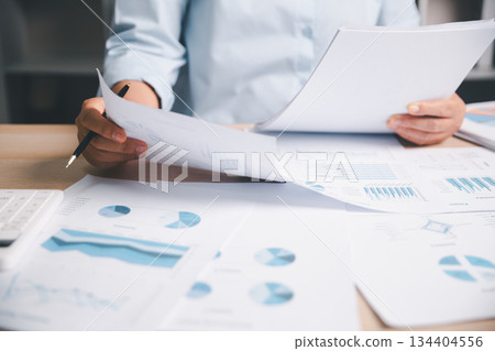 Business professional reviewing multiple financial documents analyzing charts reports desk illustrating financial planning accounting workflow data analysis corporate strategy performance evaluation 134404556