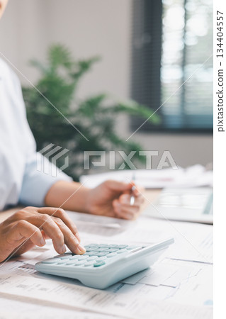 Close-up of office worker calculating financial figures with calculator while writing notes in notebook, illustrating budgeting, expense management, accounting tasks, professional financial workflow. 134404557