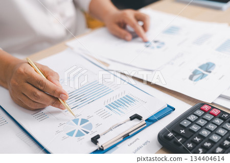 Close up of businessperson analyzing financial chart and graph with pen and calculator on desk, concept of accounting management, budget planning, financial report and data analysis. Close up of businessperson analyzing financial chart and graph with pen and calculator on desk, concept of accounting management, budget planning, financial report and data analysis. 134404614