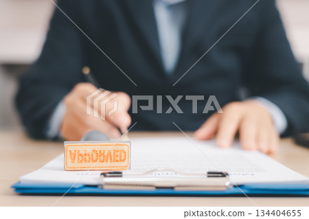 Businessman signing and stamping official document at desk, concept of legal contract approval, authorization or business agreement confirmation in corporate office background. stamp approval Businessman signing and stamping official document at desk, concept of legal contract approval, authorization or business agreement confirmation in corporate office background. stamp approval 134404655