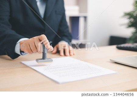 Businessman signing and stamping official document at desk, concept of legal contract approval, authorization or business agreement confirmation in corporate office background. stamp approval 134404656