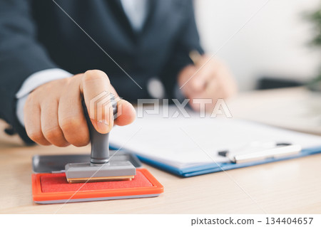 Businessman signing and stamping official document at desk, concept of legal contract approval, authorization or business agreement confirmation in corporate office background. stamp approval Businessman signing and stamping official document at desk, concept of legal contract approval, authorization or business agreement confirmation in corporate office background. stamp approval 134404657
