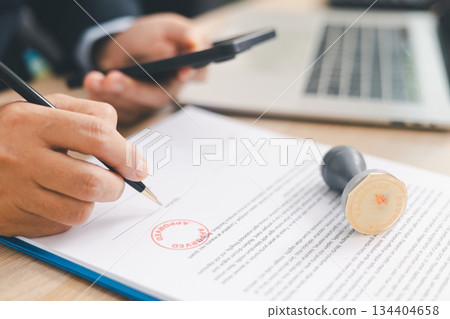 Businessman signing and stamping official document at desk, concept of legal contract approval, authorization or business agreement confirmation in corporate office background. stamp approval Businessman signing and stamping official document at desk, concept of legal contract approval, authorization or business agreement confirmation in corporate office background. stamp approval 134404658