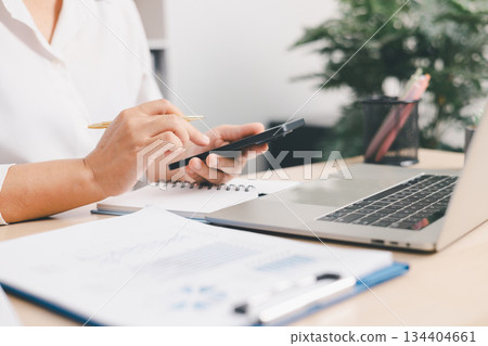 Businessperson using smartphone and laptop with financial documents on office desk, concept of online communication, finance management, digital business and data analysis workflow. Businessperson using smartphone and laptop with financial documents on office desk, concept of online communication, finance management, digital business and data analysis workflow. 134404661