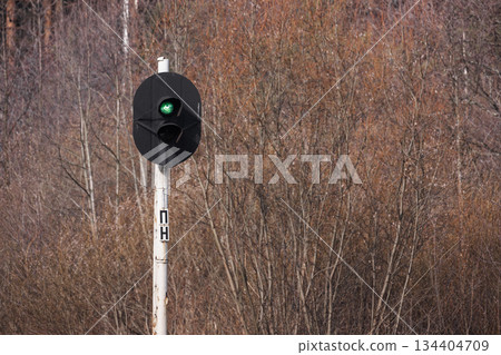 A lone railway signal with a green light stands against a backdrop of leafless trees 134404709