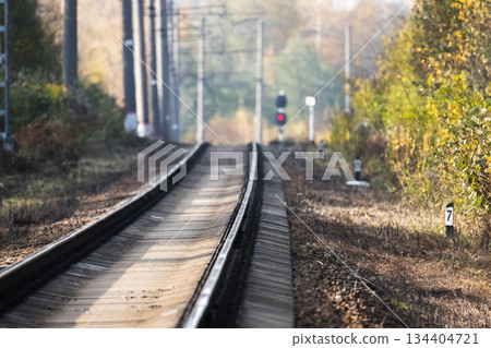 A serene railway line winds through an autumn landscape, red light is in distance A serene railway line winds through an autumn landscape, red light is in distance 134404721