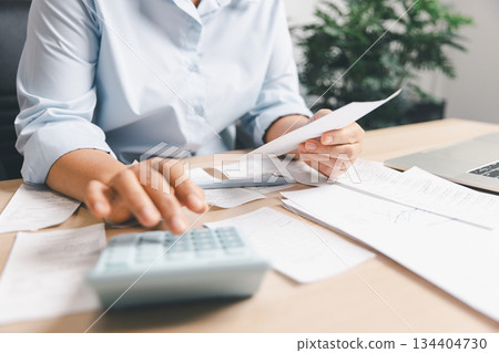 Business person calculating expenses and reviewing receipts at a desk, illustrating financial planning, bill payment, accounting workflow, budgeting, cost management and daily office finance tasks. 134404730