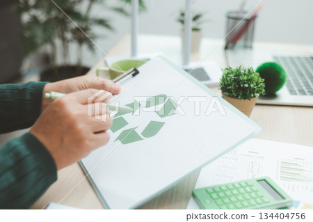 Business person holding recycle symbol on clipboard with green charts on desk, representing circular economy, eco responsibility, sustainability and environmental business concept. 134404756