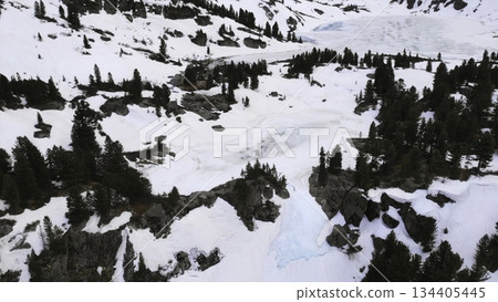 Snowy mountain valley panning showing partially frozen lake and pine trees. Media 134405445