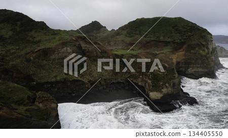 Ocean waves crashing against rocky coastline on cloudy day Ocean waves crashing against rocky coastline on cloudy day 134405550
