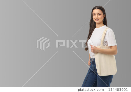Woman smiles while holding a tote bag against a gray backdrop 134405901