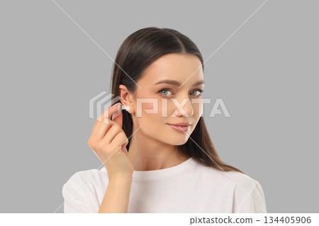 A woman shows how to wear a wireless earbud in a backdrop 134405906