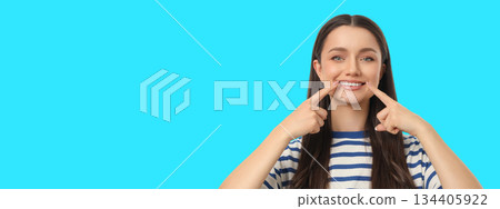 Woman points at her smile on a bright blue backdrop Woman points at her smile on a bright blue backdrop 134405922