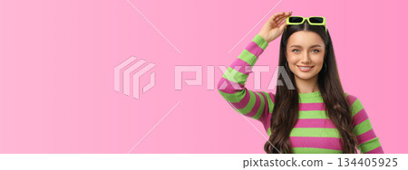 Young woman smiles and adjusts her sunglasses in bright light 134405925